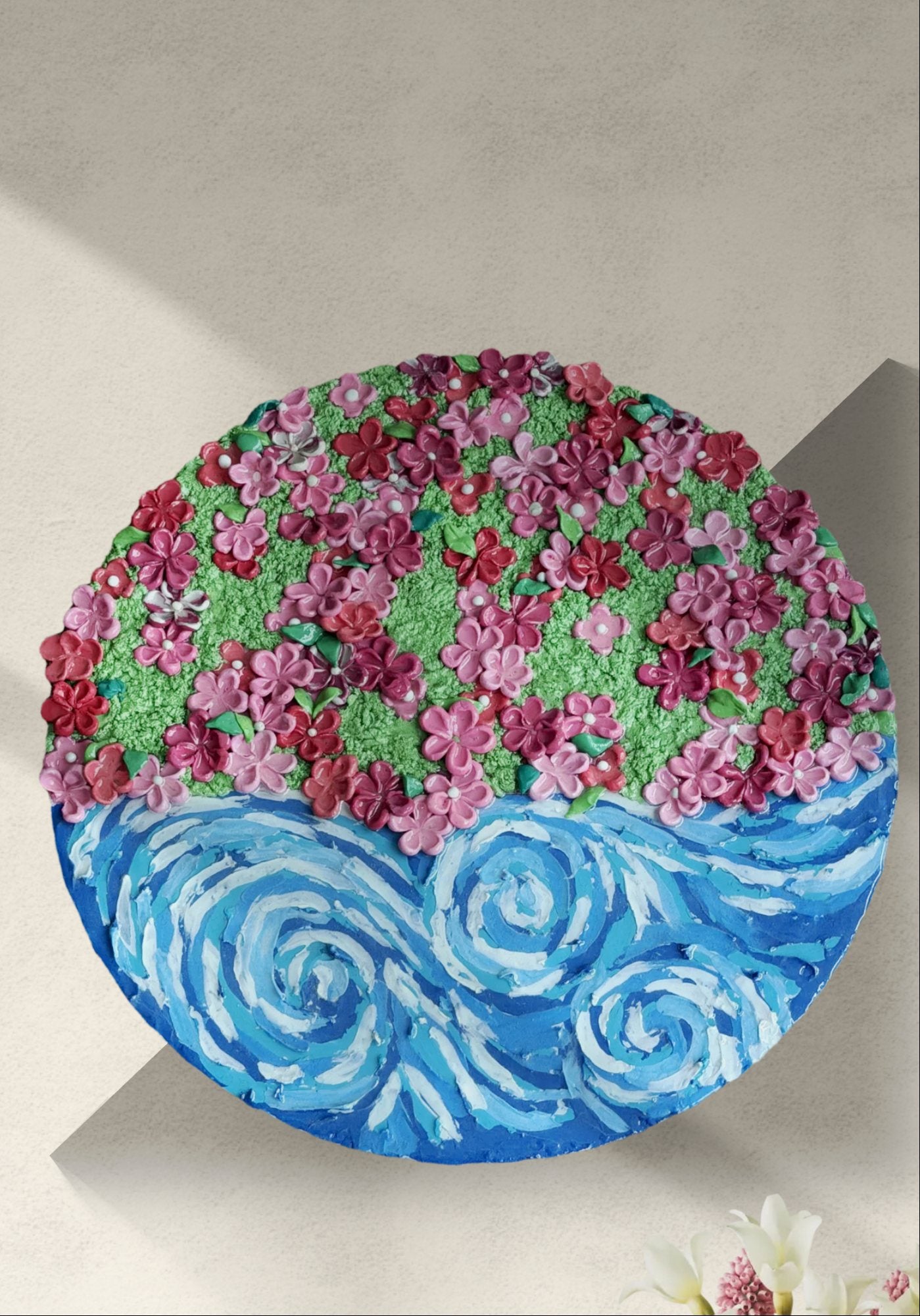Round mixed-media painting with layered pink blossoms above swirling blue waves