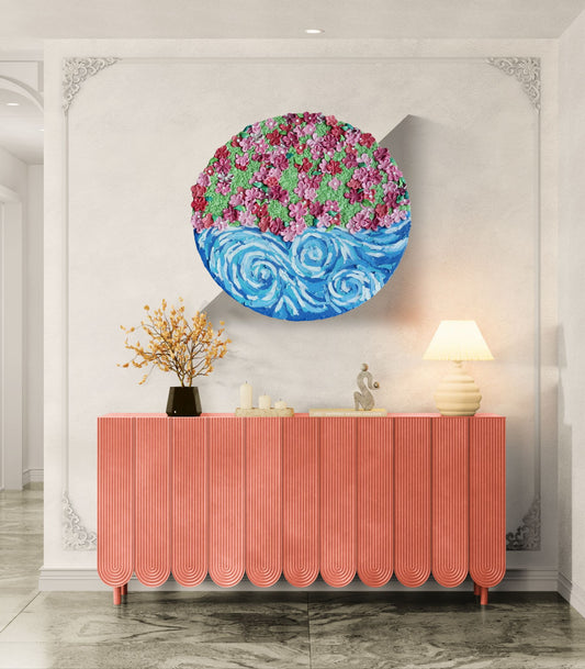 The Art of Flow — round mixed-media artwork above a coral console; raised pink and magenta clay flowers over a swirling blue current.